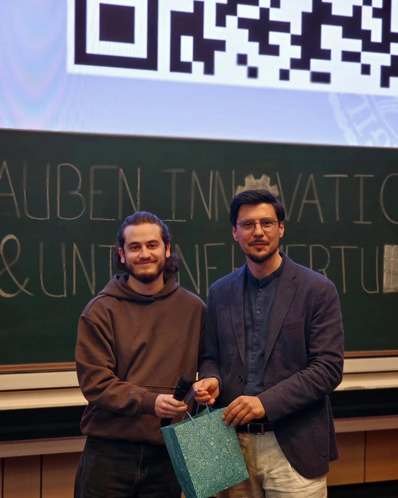 Zwei Männer posieren lächelnd mit einem Geschenk in der Hand