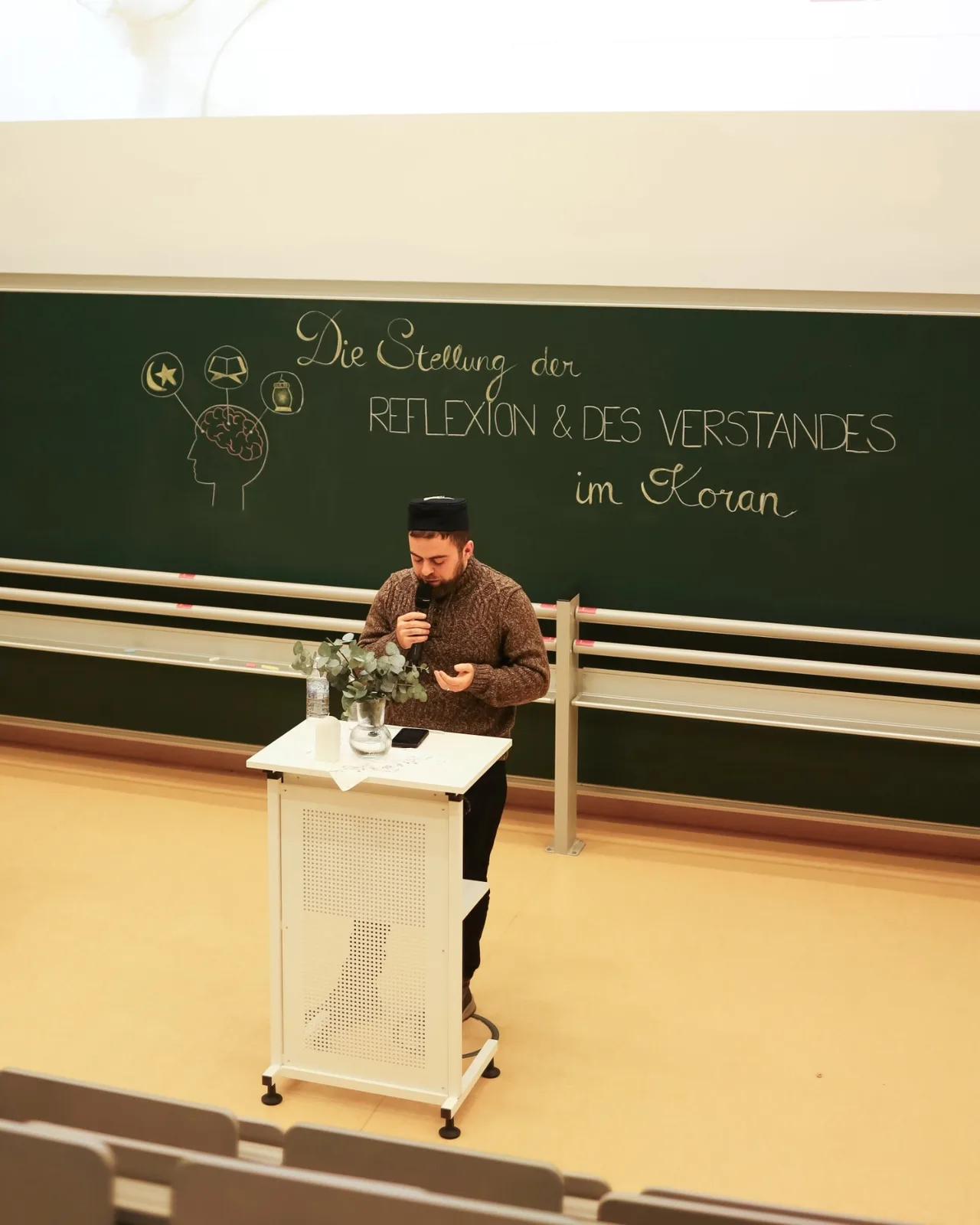 Redner steht am Stehpult vor der Tafel Die Stellung der Reflexion