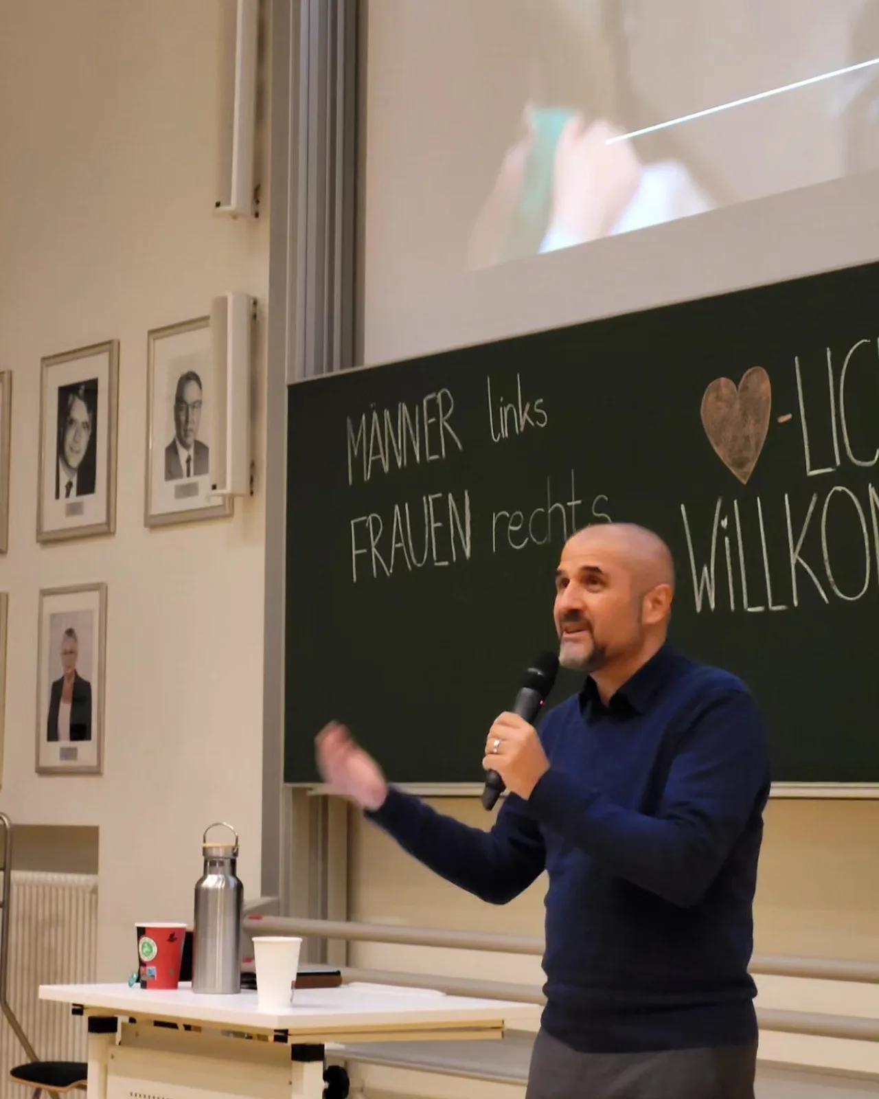 Referent gestikuliert vor einer Tafel mit Willkommensbotschaft