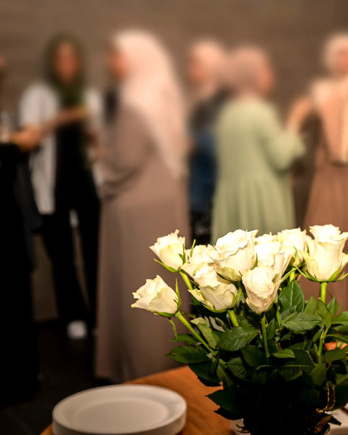 Weiße Rosen auf einem Tisch, im Hintergrund unscharf eine Gruppe Schwestern im Gespräch.