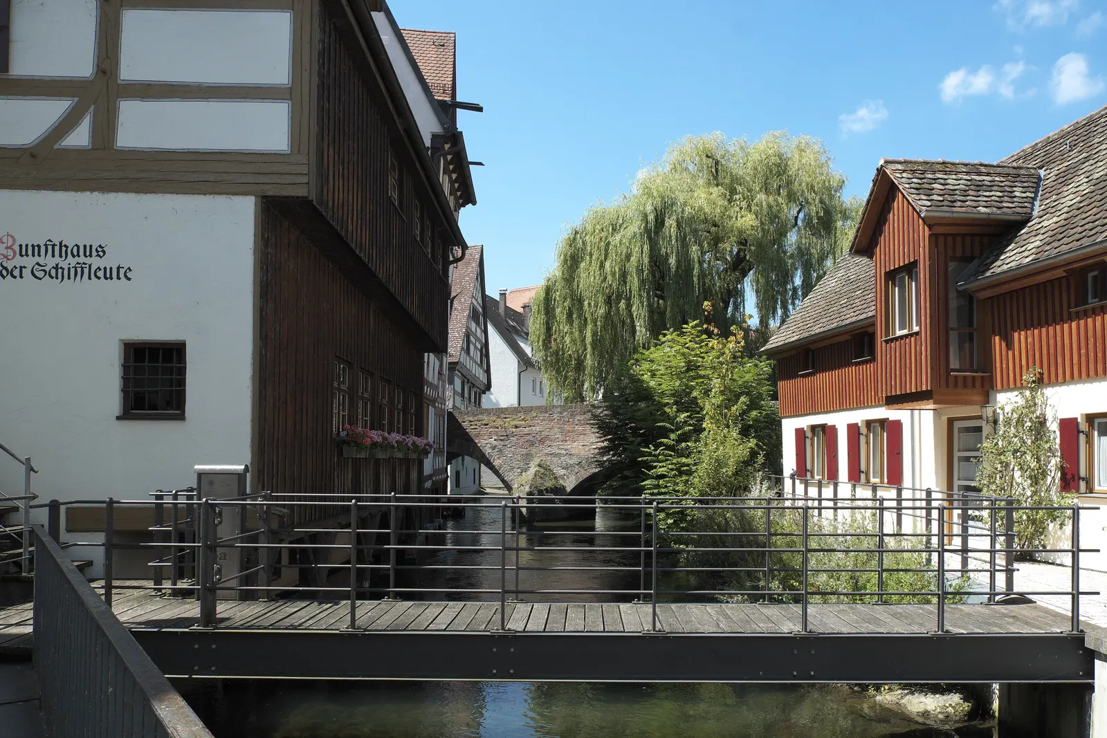 Ein Steg über die Blau zwischen alten Handwerkerhäusern im Fischerviertel, dahinter eine Trauerweide
