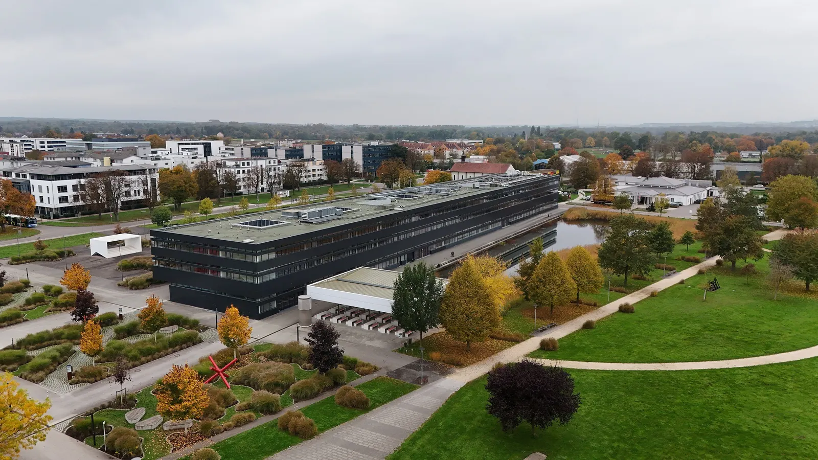 Luftaufnahme der Hochschule Neu-Ulm mit dunklem Hauptgebäude, Gärten und den Wohnvierteln dahinter