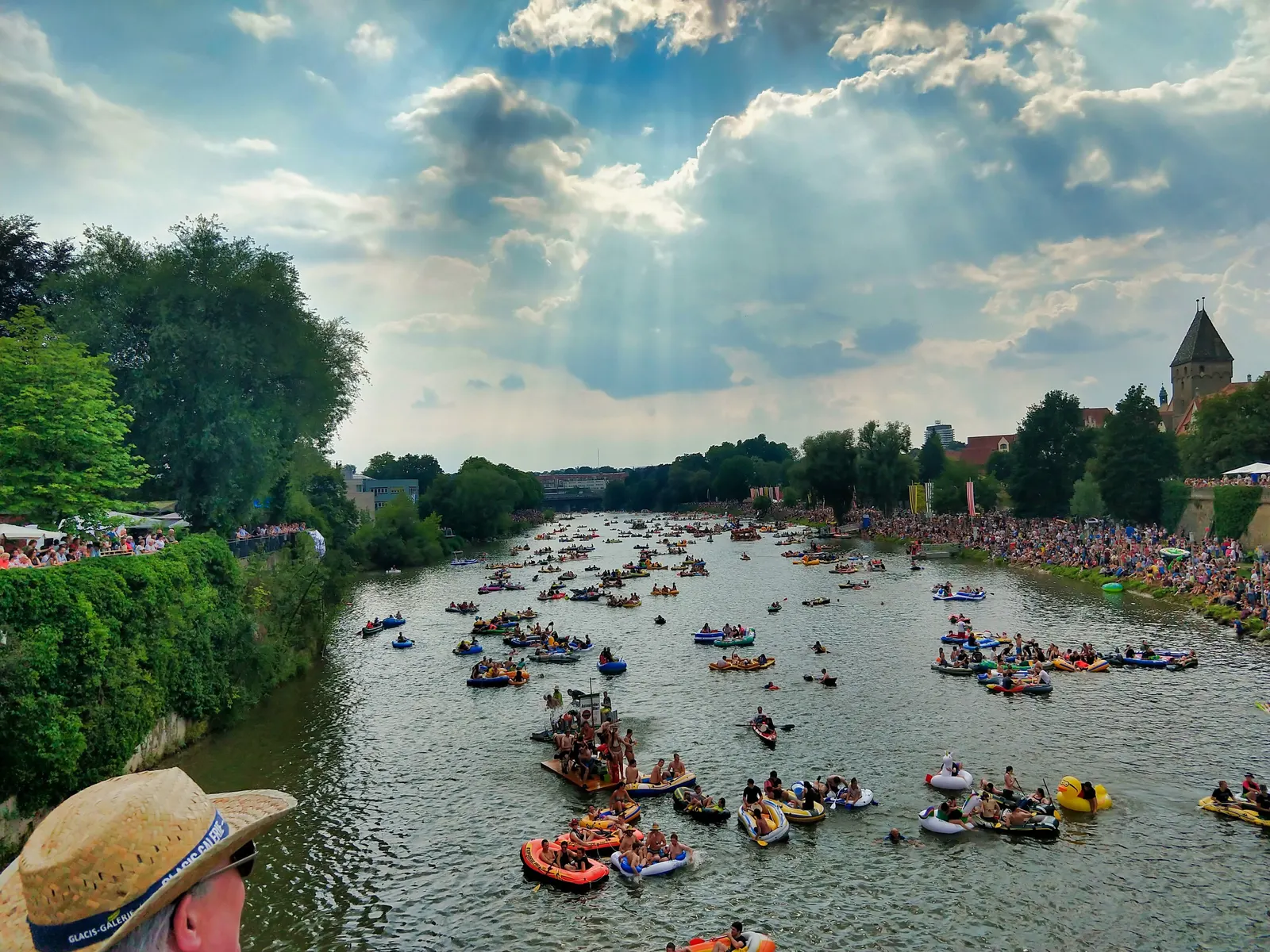 Hunderte Boote und Schwimmreifen treiben beim Nabada am Schwörmontag die Donau hinunter, an den Ufern stehen Zuschauer