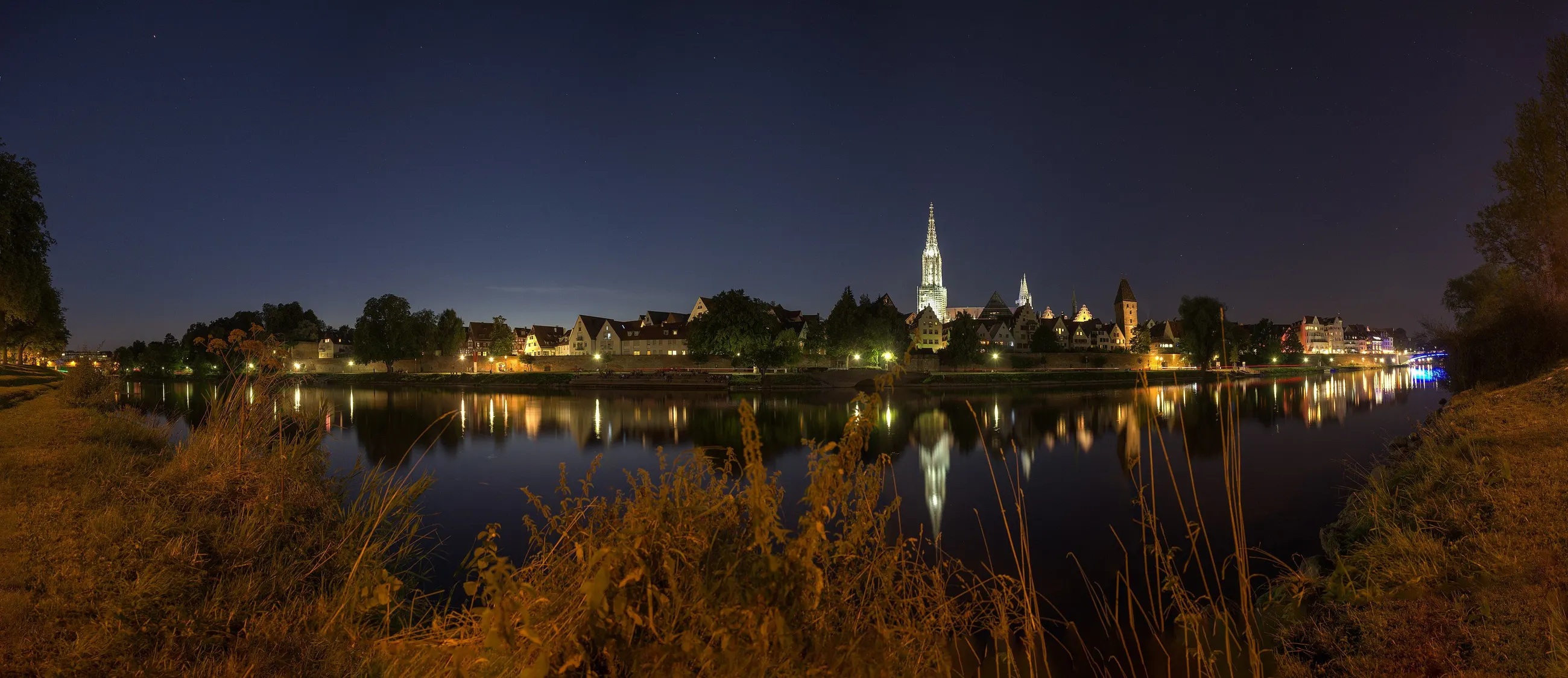 Nachtpanorama: Die Lichter von Ulm und das beleuchtete Münster spiegeln sich in der Donau